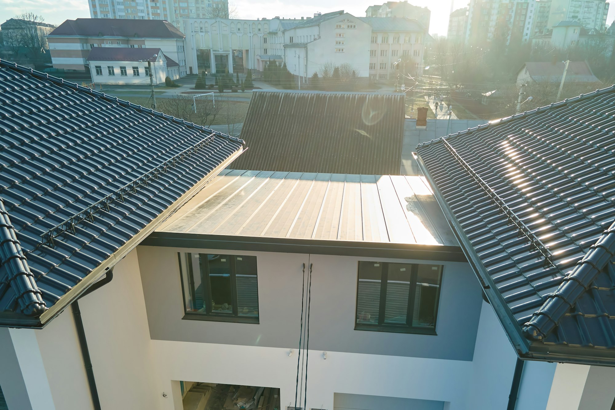 Closeup of house roof top covered with ceramic shingles with gutter pipes for rain water.