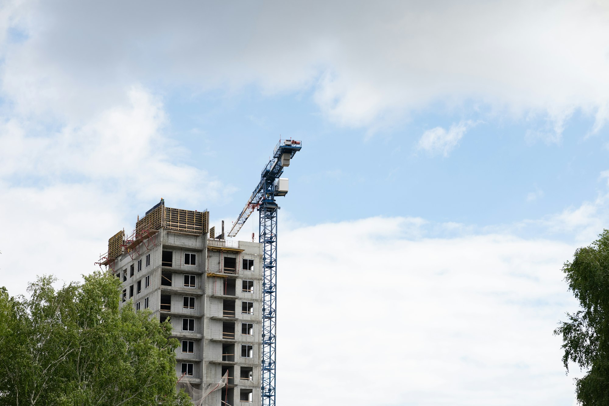 View of the unfinished wall of the house. A construction crane on a blue sky background.